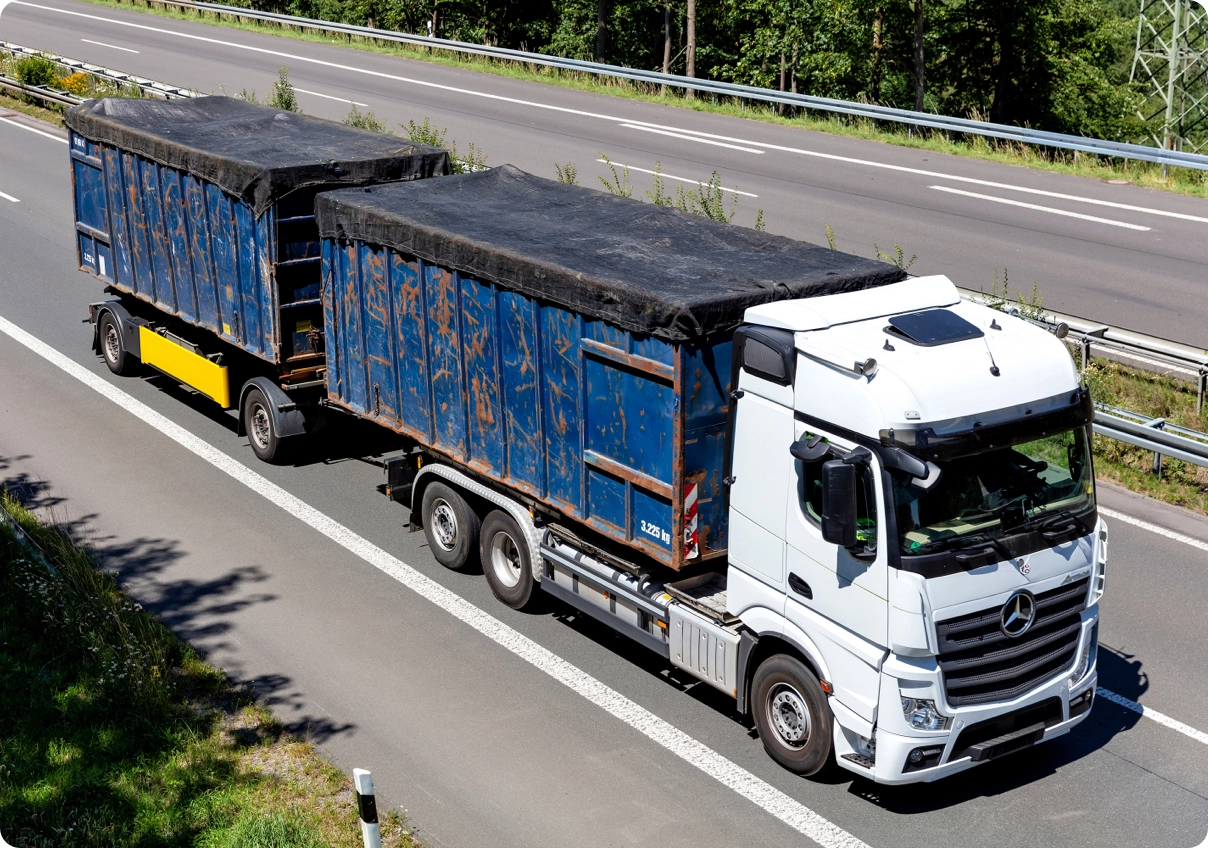 A ScrapIT-tracked truck hauling two loaded scrap trailers along a highway.